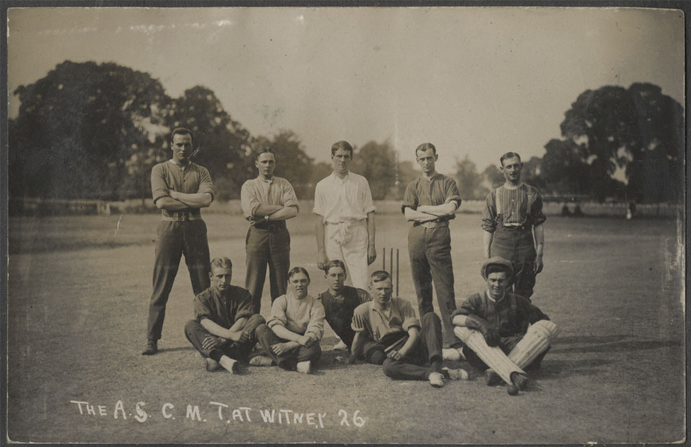 Black and white photograph of a group of young white men in vintage sporting clothing posing seated or standing on a cricket field, with cricket equipment