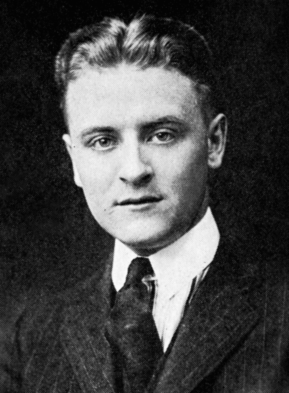 Black and white newsprint portrait photo of a young white man with short pomaded hair wearing a suit and tie