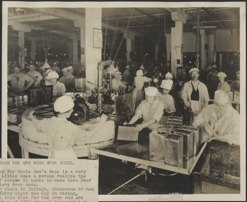 Black and white photograph showing a factory floor covered in tables and machinery, with lots of uniformed workers performing tasks