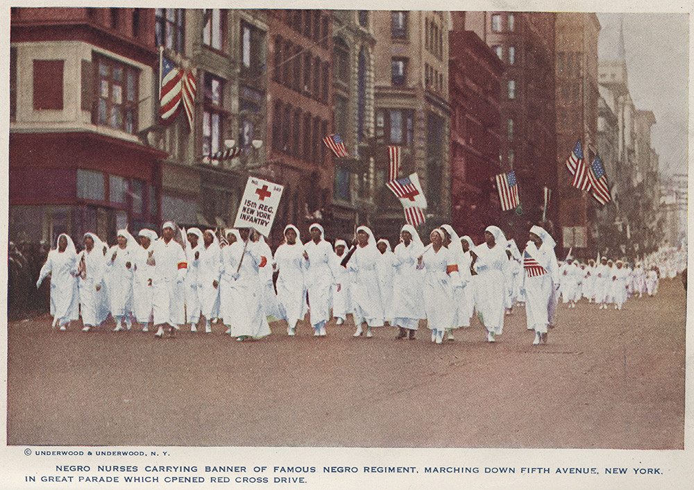 Colorized photograph of a large group of Black women nurses dressed in white uniforms marching down a city street