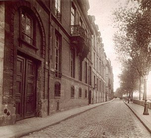 Sepia photograph of a Parisian city block. Brick building façades stretch away into the distance.