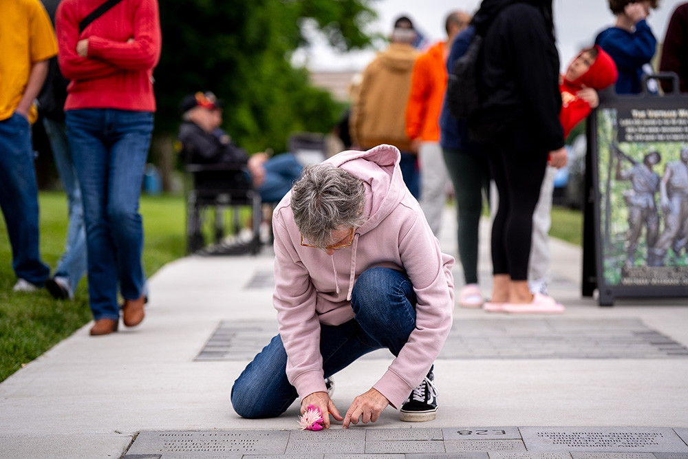 Person wearing a pink sweatshirt and jeans kneeling by a display of engraved bricks embedded in a sidewalk