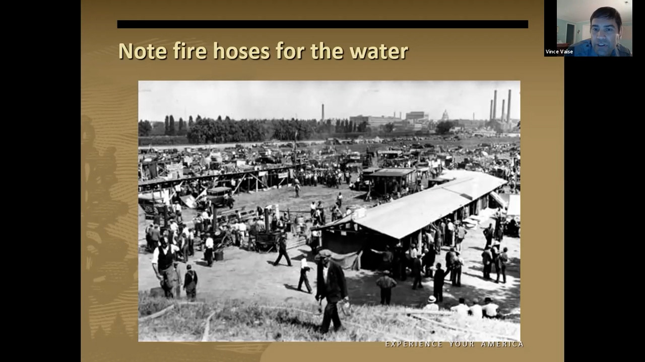 View of the shantytown from a hill. In the foreground, a man stands on the slope of the hill with hoses snaking down the hill.