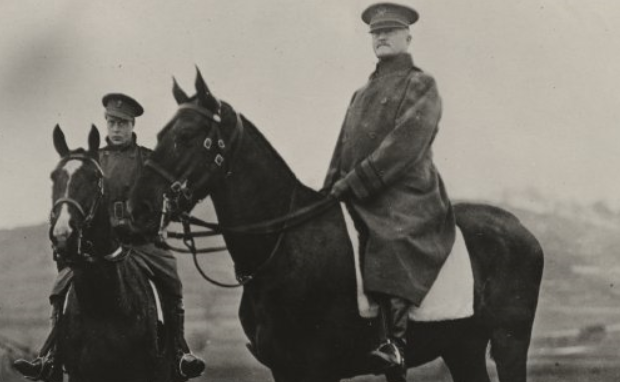Black and white photo of two men dressed in cold weather uniforms, wearing hats and sitting on top of horses. The man central in the image is General Pershing.