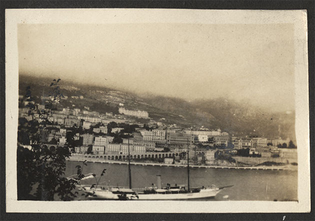 Black and white photo of a harbor or channel with houses in the background and a sailing yacht in the foreground