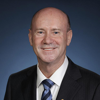 Portrait photo of a bald white man wearing a black suit and blue tie